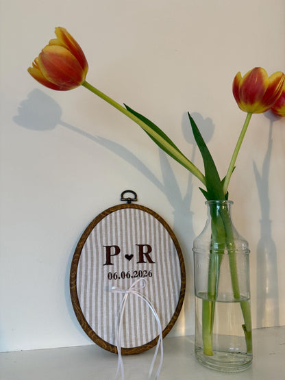 Embroidery hoop on striped fabric with P.R initials, 06.06.2026 date, white ribbon ties.