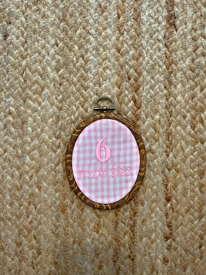 Hanging oval '6 months' milestone disc with pink gingham background