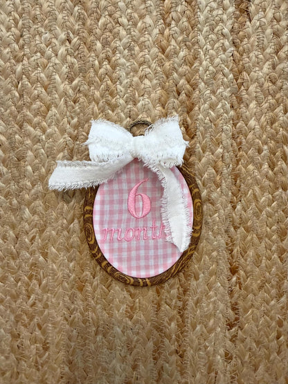 Pink gingham oval milestone patch with bow, showing '6 months'