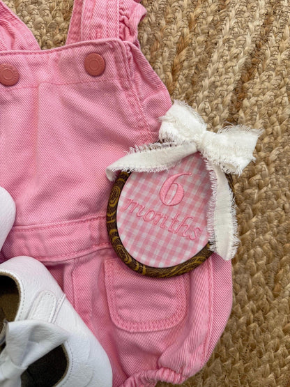 Pink gingham baby romper with bow, oval milestone patch and white lace trim