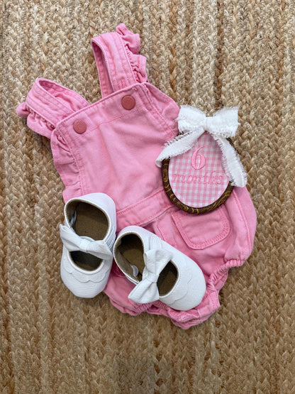 Pink gingham baby romper with bow, white baby shoes, and oval '6 months' patch