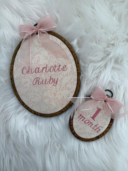 Two pink floral oval name signs with pink bows, embroidered baby names on faux fur